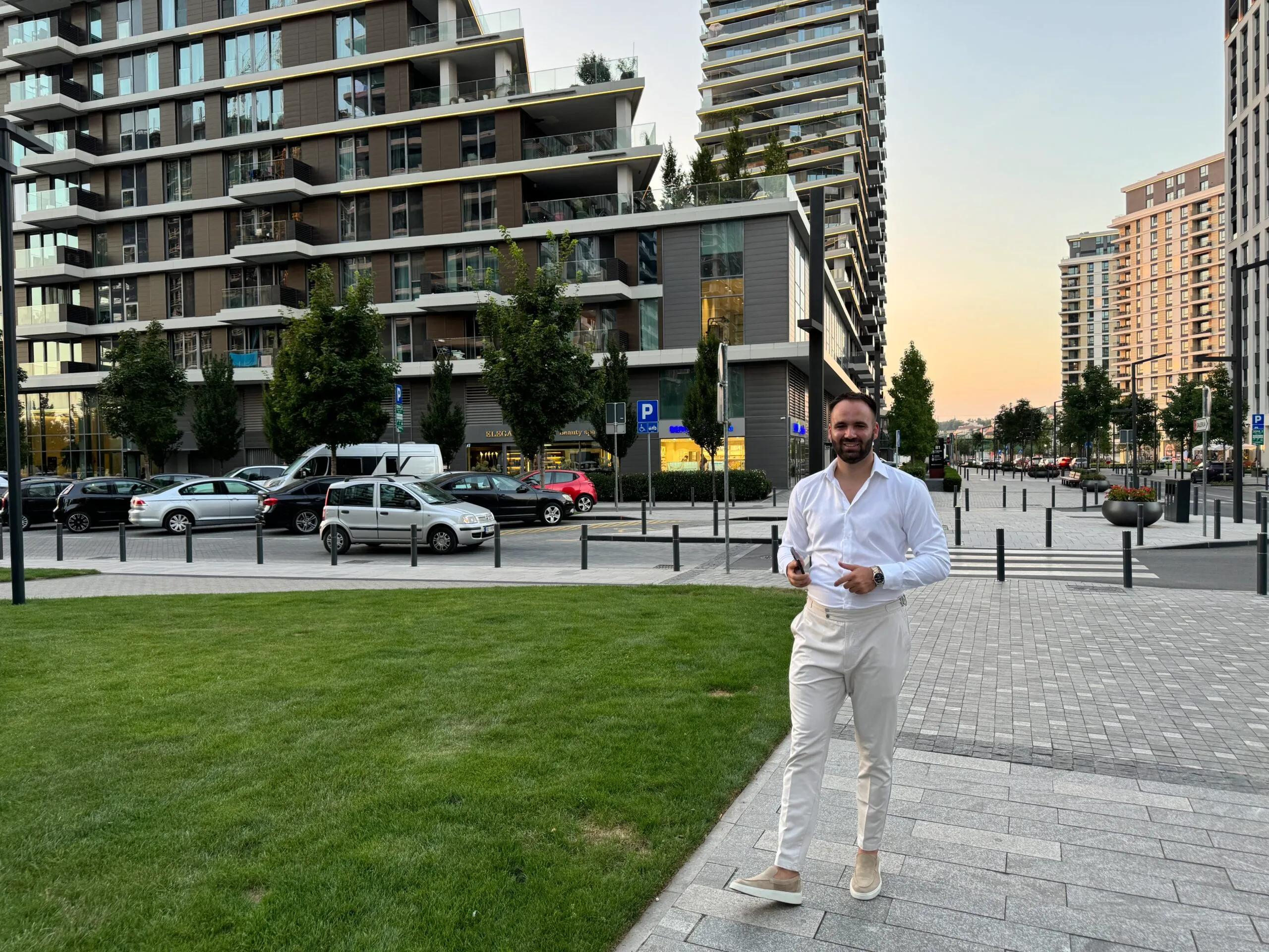 Agent za nekretnine stoji ispred modernih zgrada u Beogradu, spreman za sastanak sa klijentom.